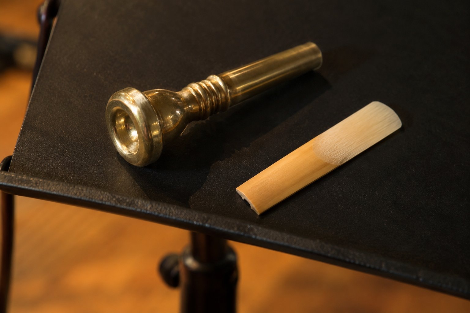 A trumpet mouthpiece and a saxophone reed on a dark music stand